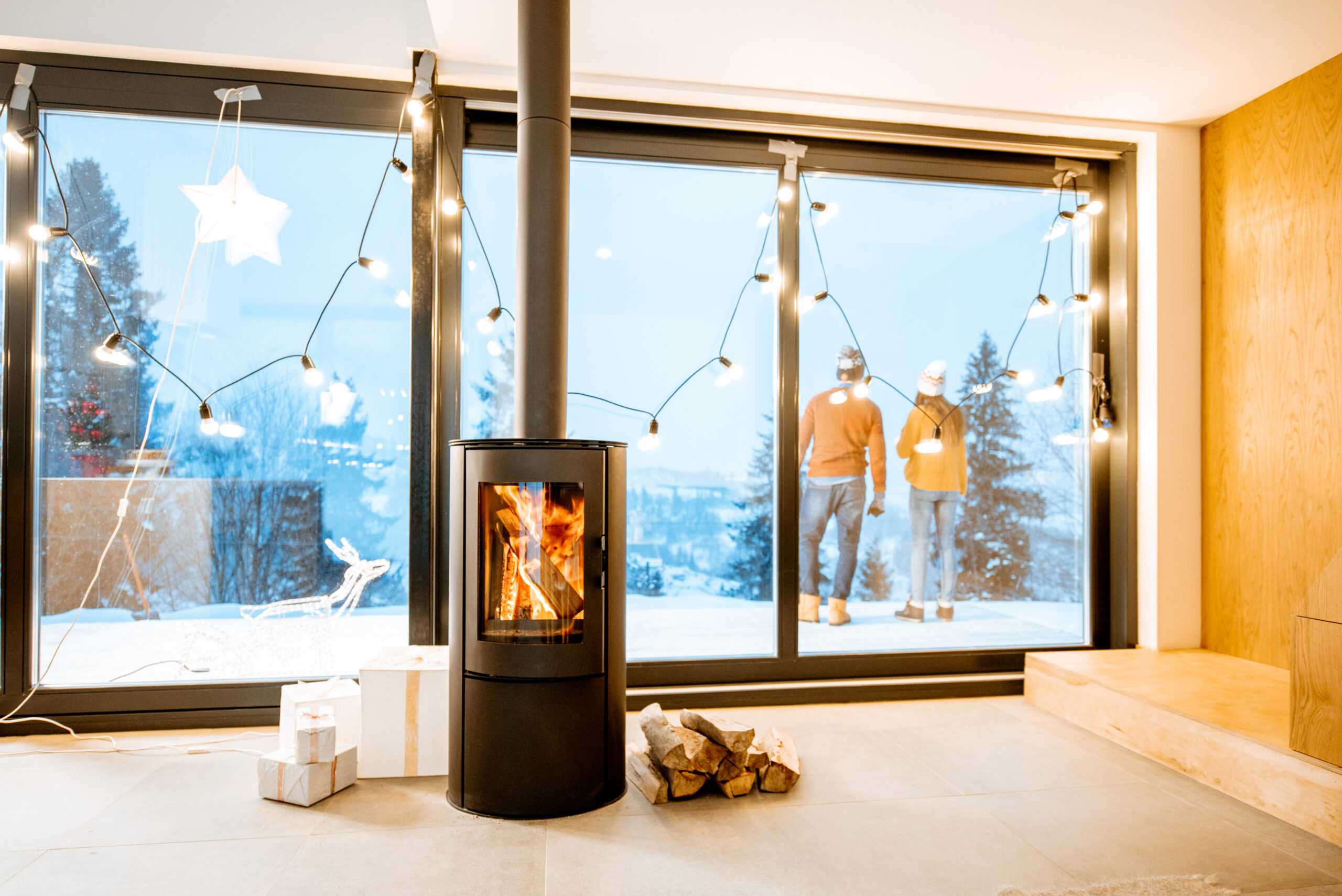 Couple standing outdoors on the terrace of the house with fireplace during the winter time. Interior view through the window